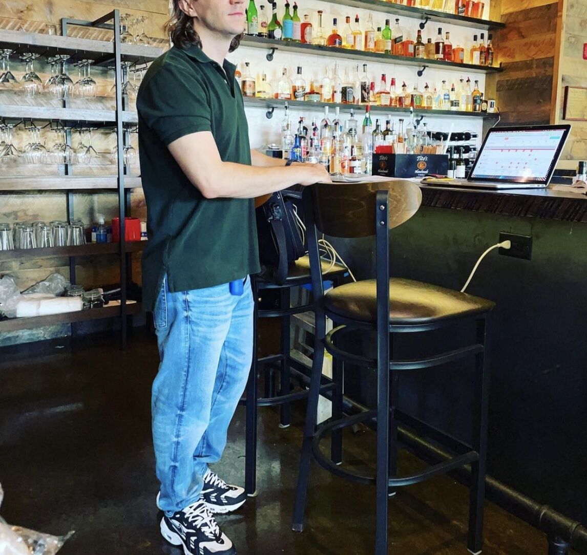 man wearing a green polo and the best dad jeans standing at a bar with a laptop on in it