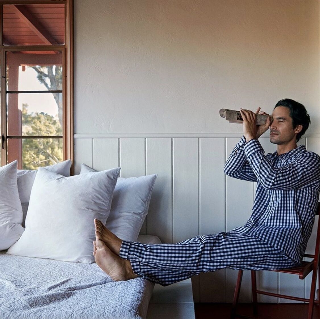 man in pajama set sitting beside the best with a rolled up newspaper looking through it like a telescope 