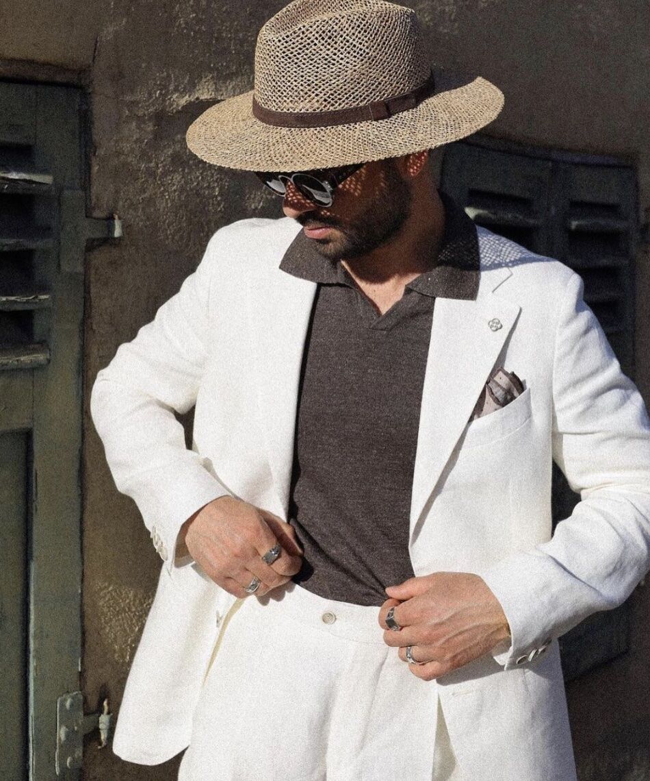 man wearing a linen suit and a straw hat, looking down, holding his pants