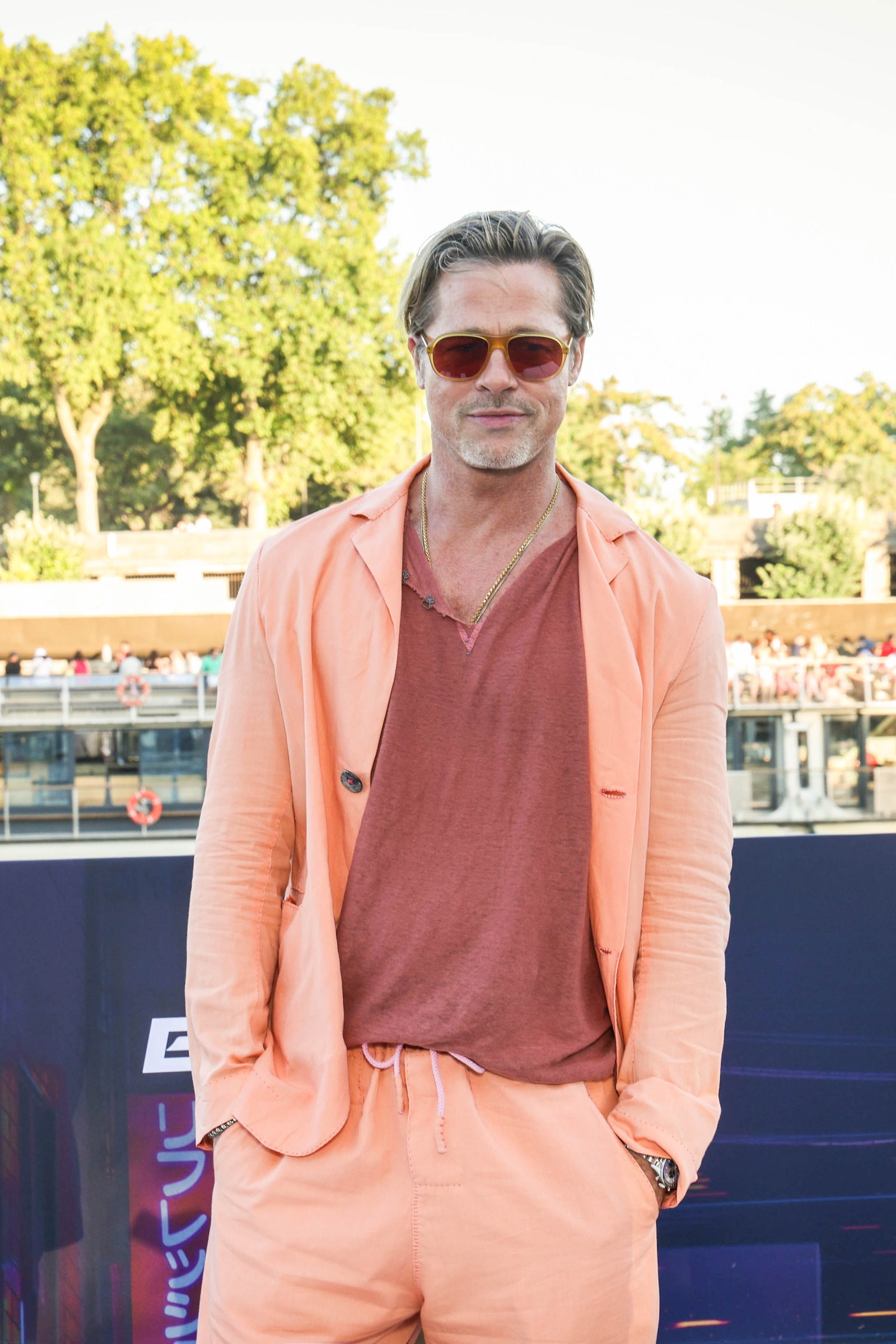 Brad Pitt wears an orange suit in front of a backdrop of trees