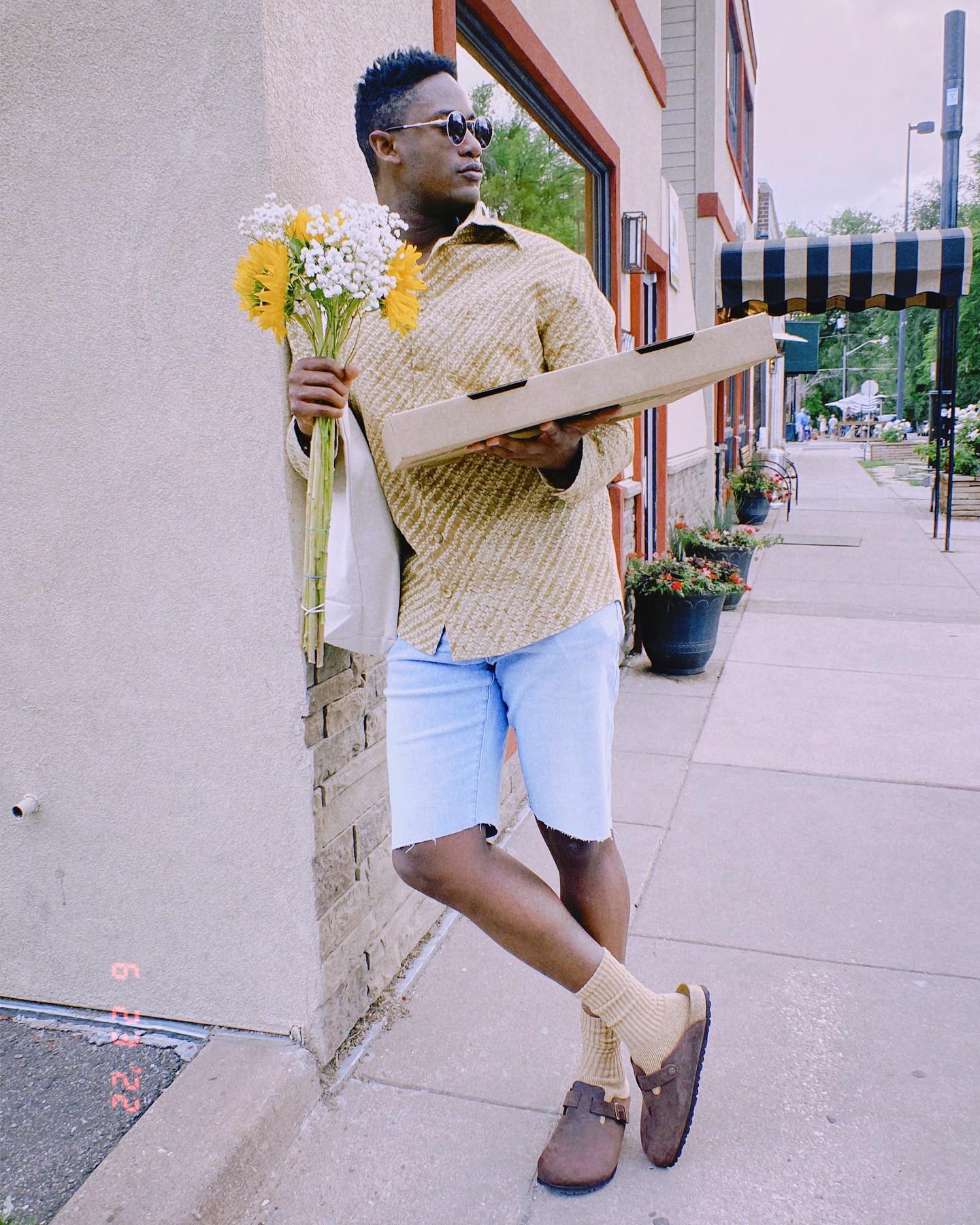 Man wearing jorts in style holding flowers and a box