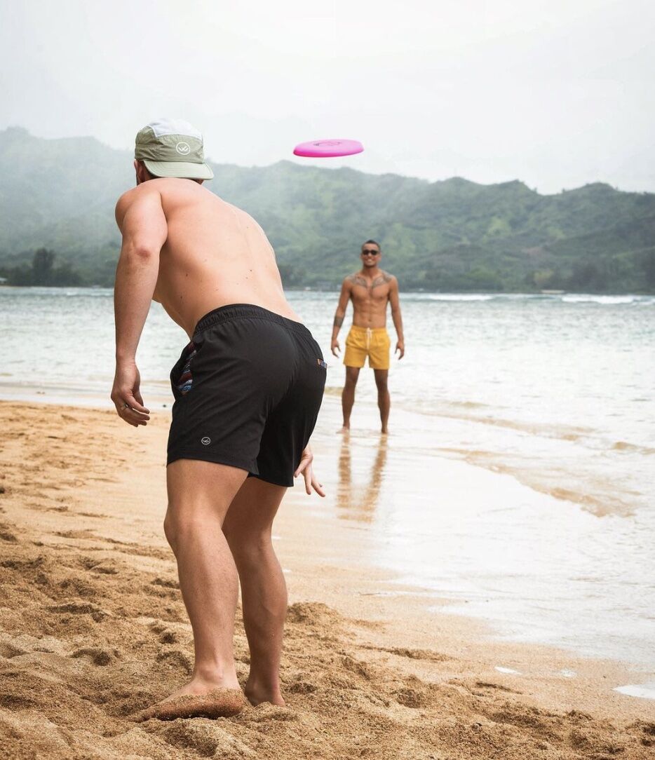 men in shorts on a beach throwing a frisbee