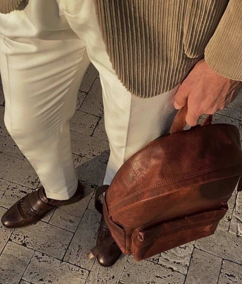 man holding a leather backpacks during the golden hour