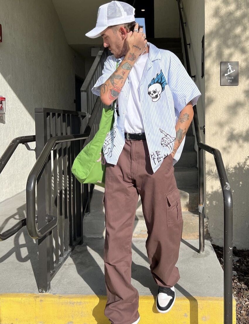 Man looking away from the camera wearing a hat, open button-up shirt and cargo pants