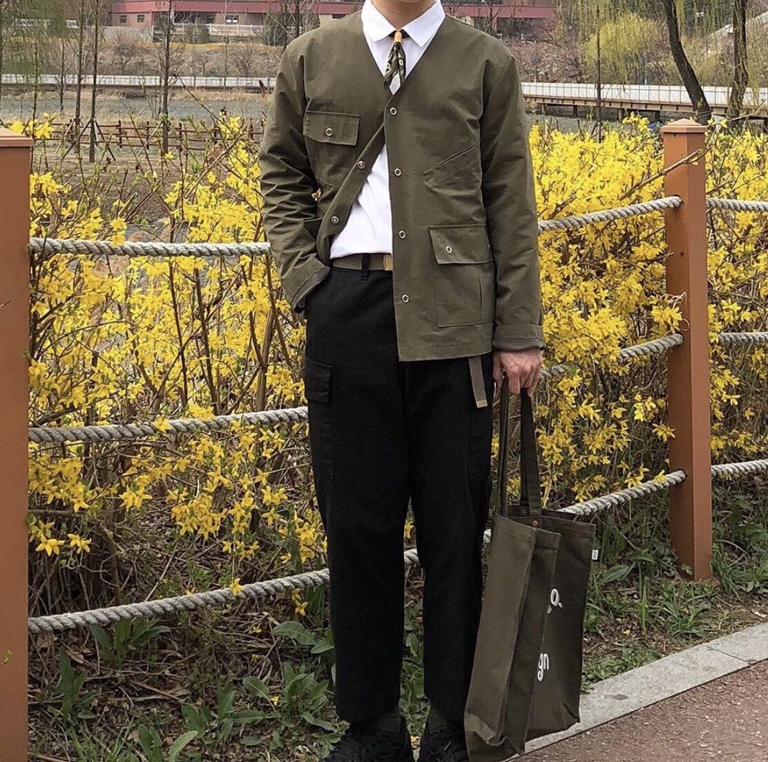 Man standing in front of flowers wearing a military belt, dress shirt and dress pants