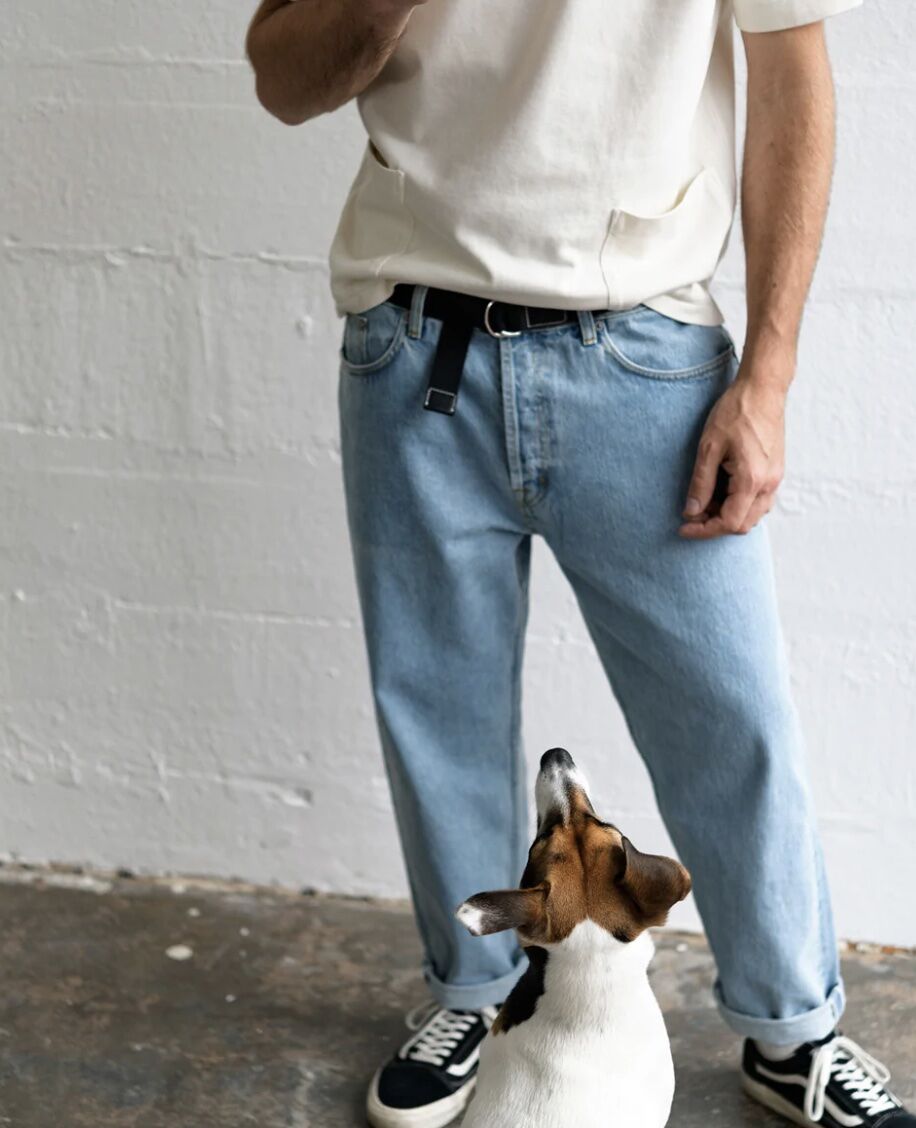 Dog sitting in front of a man wearing a d-ring belt and jeans and a t-shirt